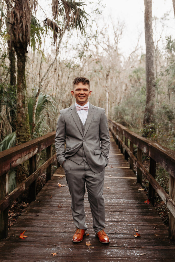 Groom in a grey suit with a pink bow tie at Highlands Hammock State Park.