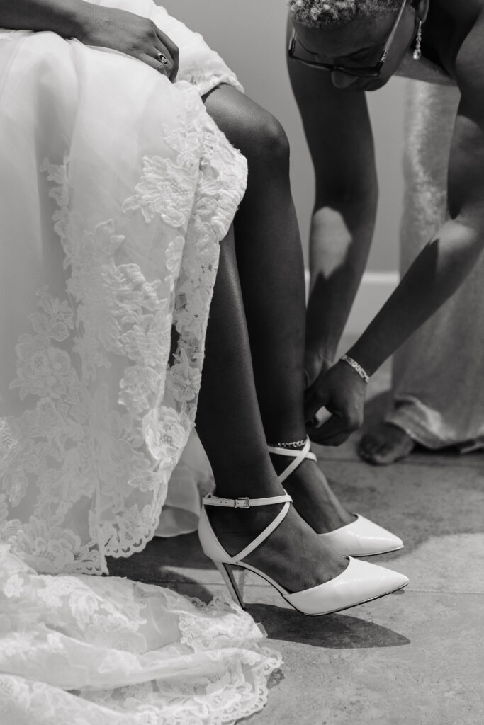 mother of bride helping bride put on her white heels