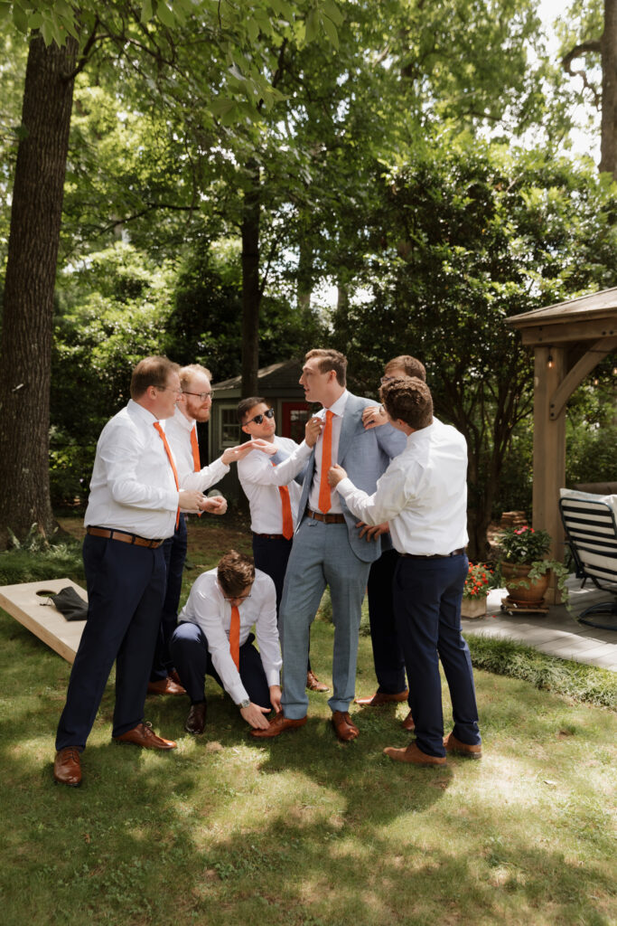 Groomsmen helping groom getting ready on his summer wedding day.