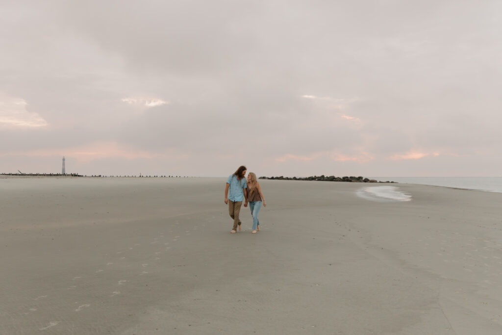 A couple walking along the beach during their sunrise engagement session at Folly Beach in Charleston, South Carolina.