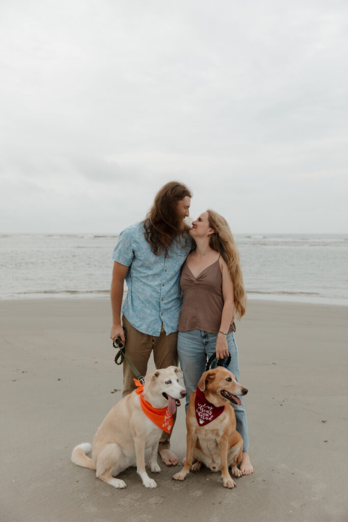 Sunrise engagement session at Folly Beach in South Carolina featuring a couple with their two dogs.