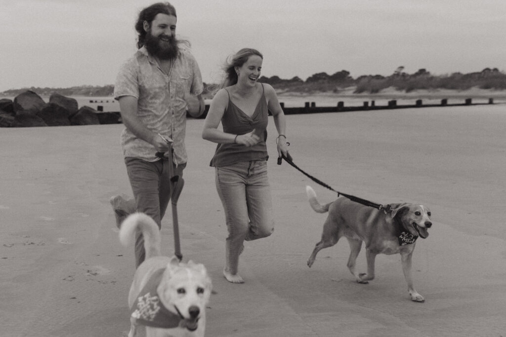 Sunrise engagement session at Folly Beach in South Carolina featuring a couple with their two dogs.