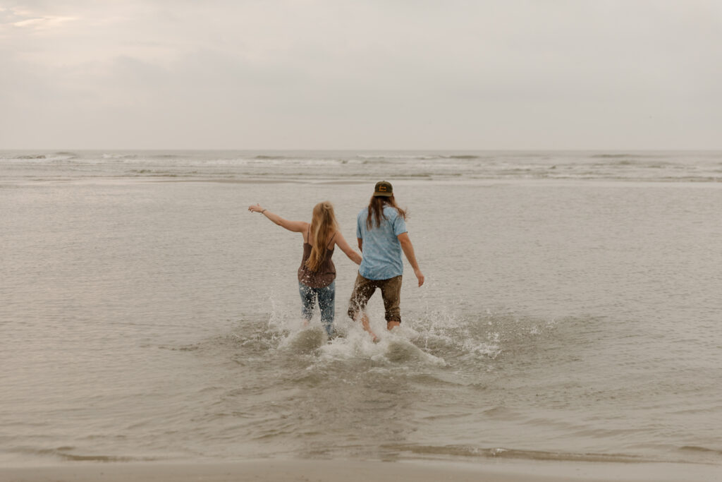 A couple running into the ocean during their sunrise engagement session at Folly Beach in South Carolina.