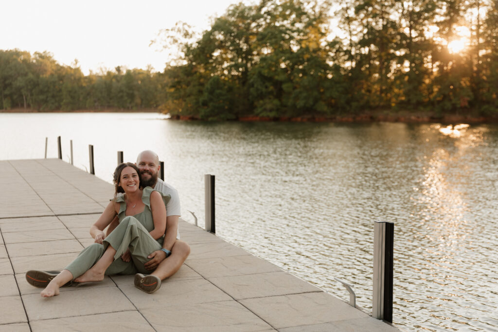 A couple sitting on a dock on Lake Keowee in South Carolina as the sun sets during their engagement session.