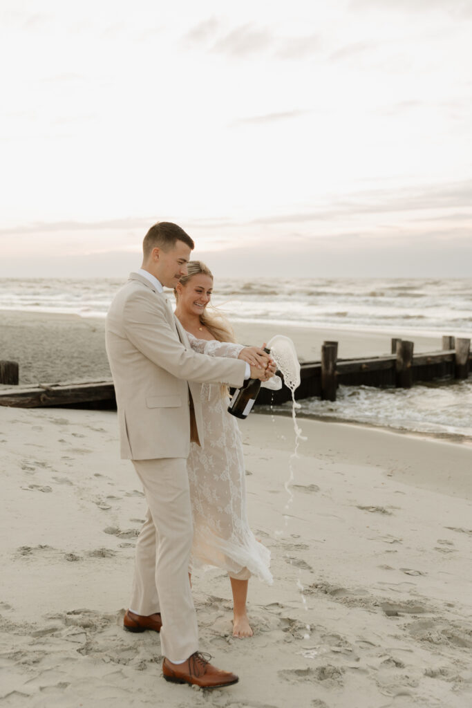 Bride and groom popping champagne during their sunrise elopement on Folly Beach in South Carolina.