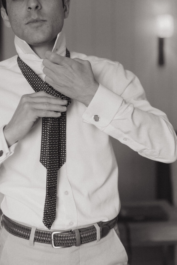 Black and white photo of a Jewish groom putting on his tie before his wedding.