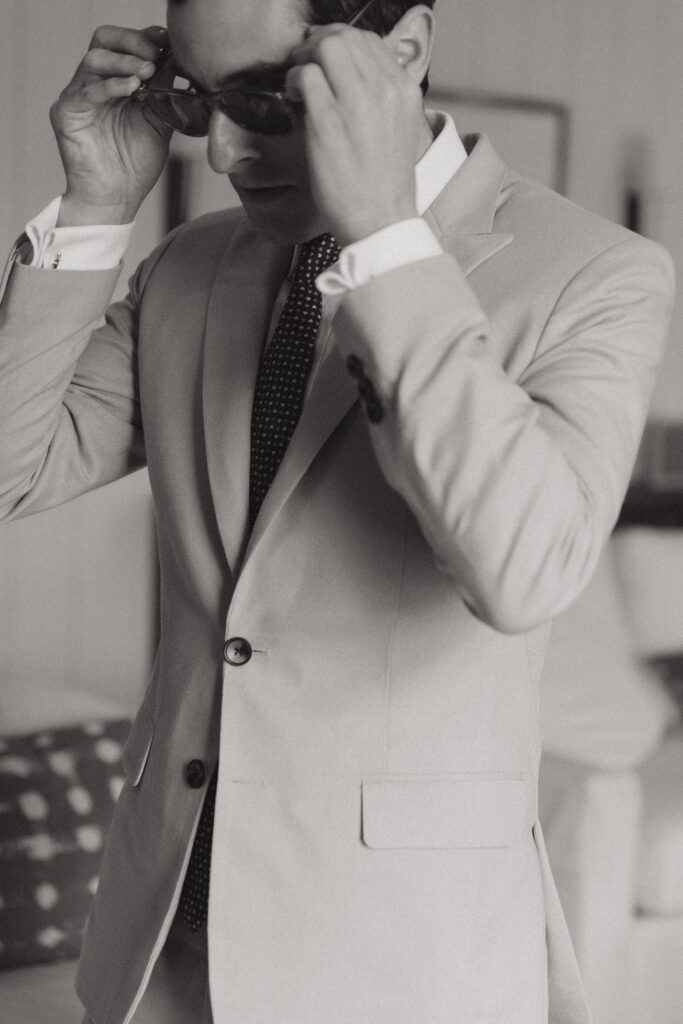 Black and white photo of a Jewish groom putting on sunglasses before his wedding.