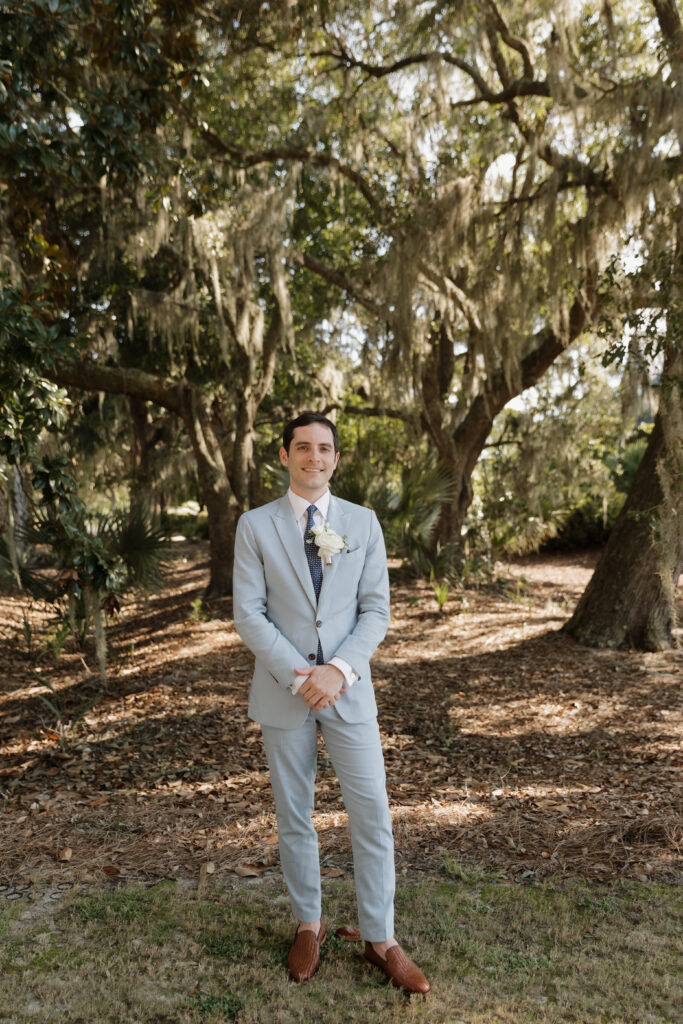 Groom wearing a light blue suit, standing under live oak trees with Spanish moss at The Golf Club at Briar's Creek on John's Island, SC.