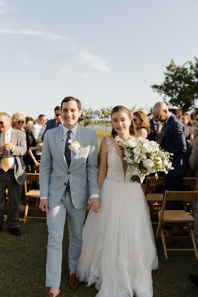 Bride and groom smiling while walking down the aisle after their Jewish wedding ceremony at The Golf Club at Briar's Creek on Johns Island, SC.