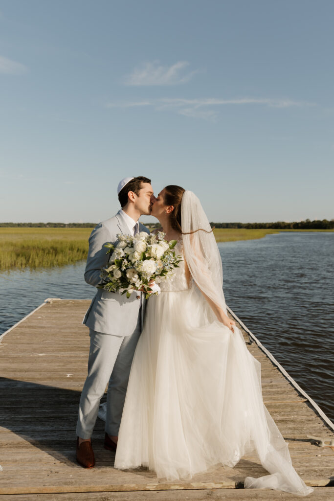 Bride and groom sharing a kiss on a dock overlooking the marsh at The Golf Club at Briar's Creek on Johns Island, SC.