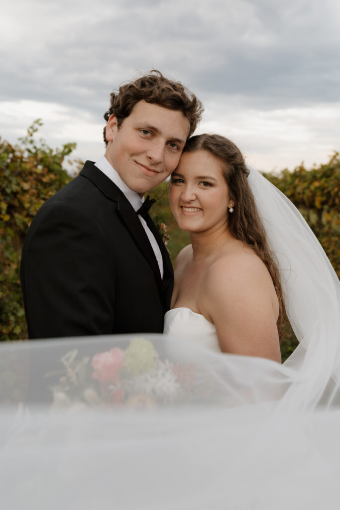 Bride and groom smiling at the camera in the vineyard at Chattooga Belle Farm in Long Creek, SC during their fall wedding day.